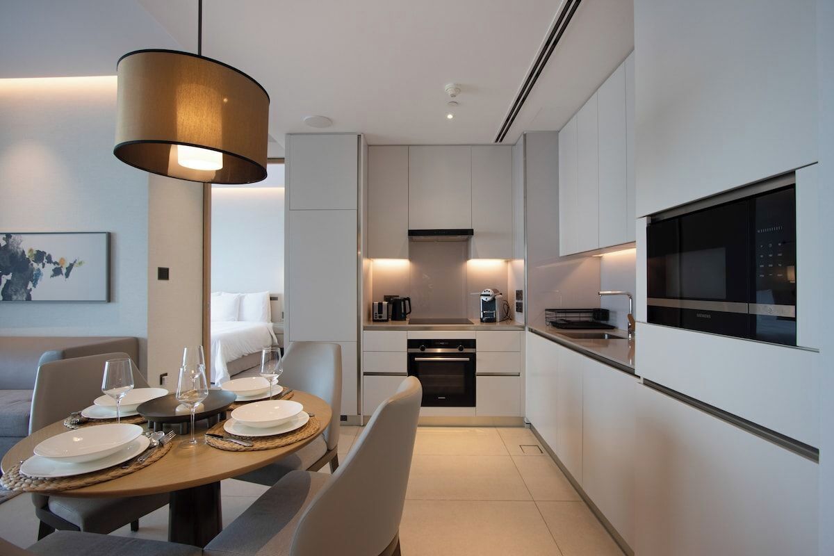 A modern kitchen with a dining area, featuring a round table set for two, a pendant light, and built-in appliances.