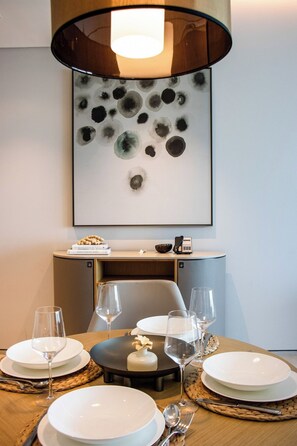 Un coin repas avec une table dressée pour quatre personnes, une lampe moderne et une œuvre d’art abstraite encadrée accrochée au mur.