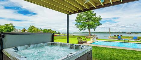 A hot tub under a covered patio with a view of a lake and a swimming pool.