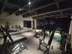 Ein Fitnessstudio mit Trainingsgeräten, Laufband und einer Gewichtshalterung.