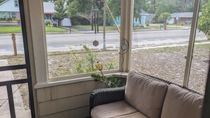 A covered porch with a cushioned seating area, a view of a residential street, and a hanging decorative item. - Charming 2-bedroom 1935 bungalow in downtown New Port Richey (New Port Richey)
