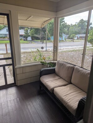 A covered porch with a cushioned seating area, a view of a residential street, and a hanging decorative item. - Charming 2-bedroom 1935 bungalow in downtown New Port Richey (New Port Richey)