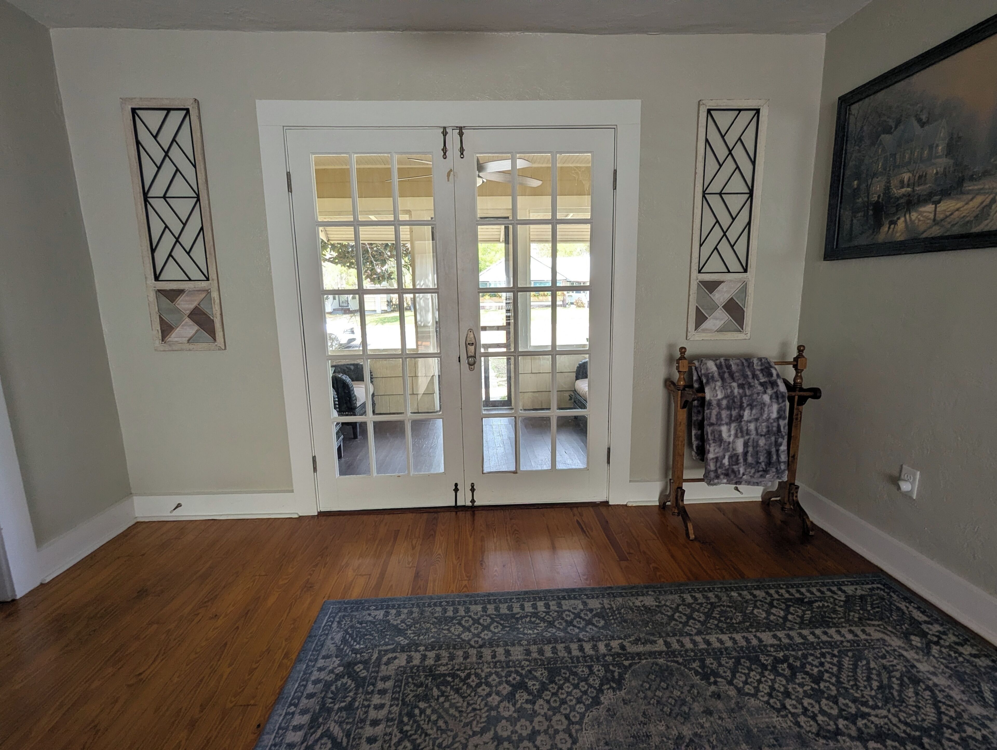 A room with a wooden floor, a patterned rug, a bench with a blanket, and a door with glass panels.