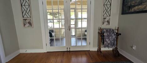 A room with a wooden floor, a patterned rug, a bench with a blanket, and a door with glass panels.