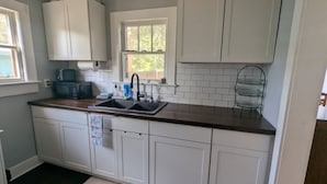 A kitchen with white cabinets, a dark countertop, a window, and a microwave. - Charming 2-bedroom 1935 bungalow in downtown New Port Richey (New Port Richey)