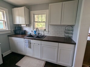 A kitchen with white cabinets, a dark countertop, a window, and a microwave. - Charming 2-bedroom 1935 bungalow in downtown New Port Richey (New Port Richey)