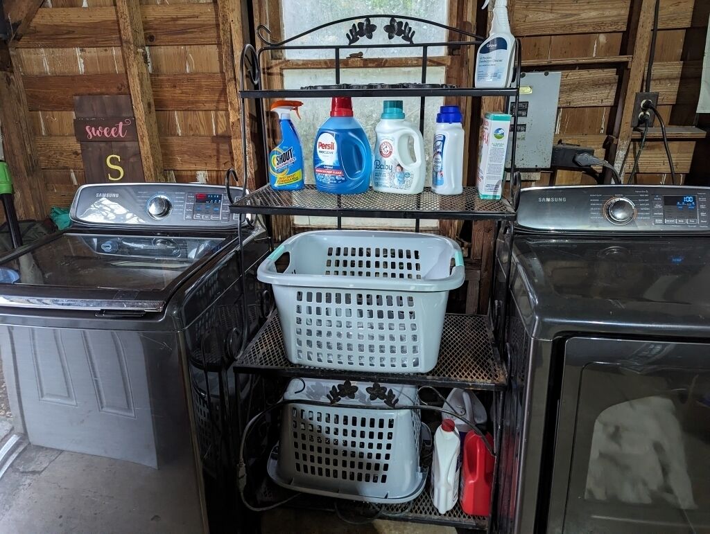A laundry area with two washing machines, a metal shelf with detergent bottles, and a sign that reads 'sweet S'.