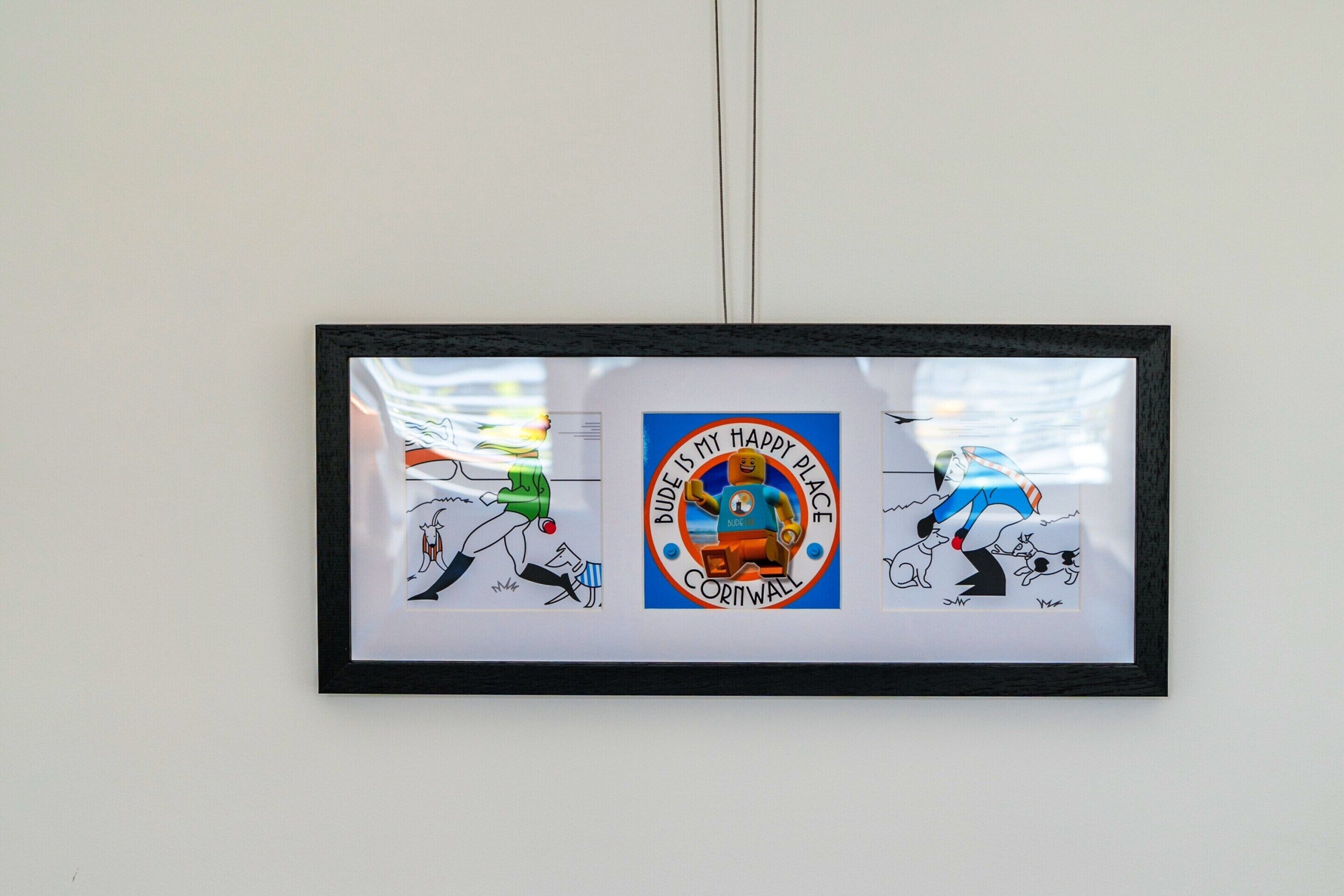 En inramad tavla med en central, cirkelformad logotyp och två illustrationer på sidorna.
