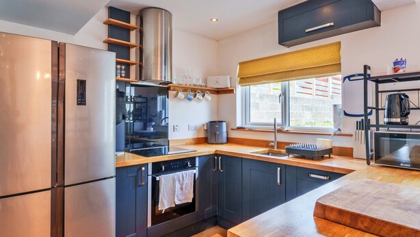 A modern kitchen with stainless steel appliances, wooden countertops, and a window with a yellow blind. - Peaceful Lochside Retreat for 4 (Bude)