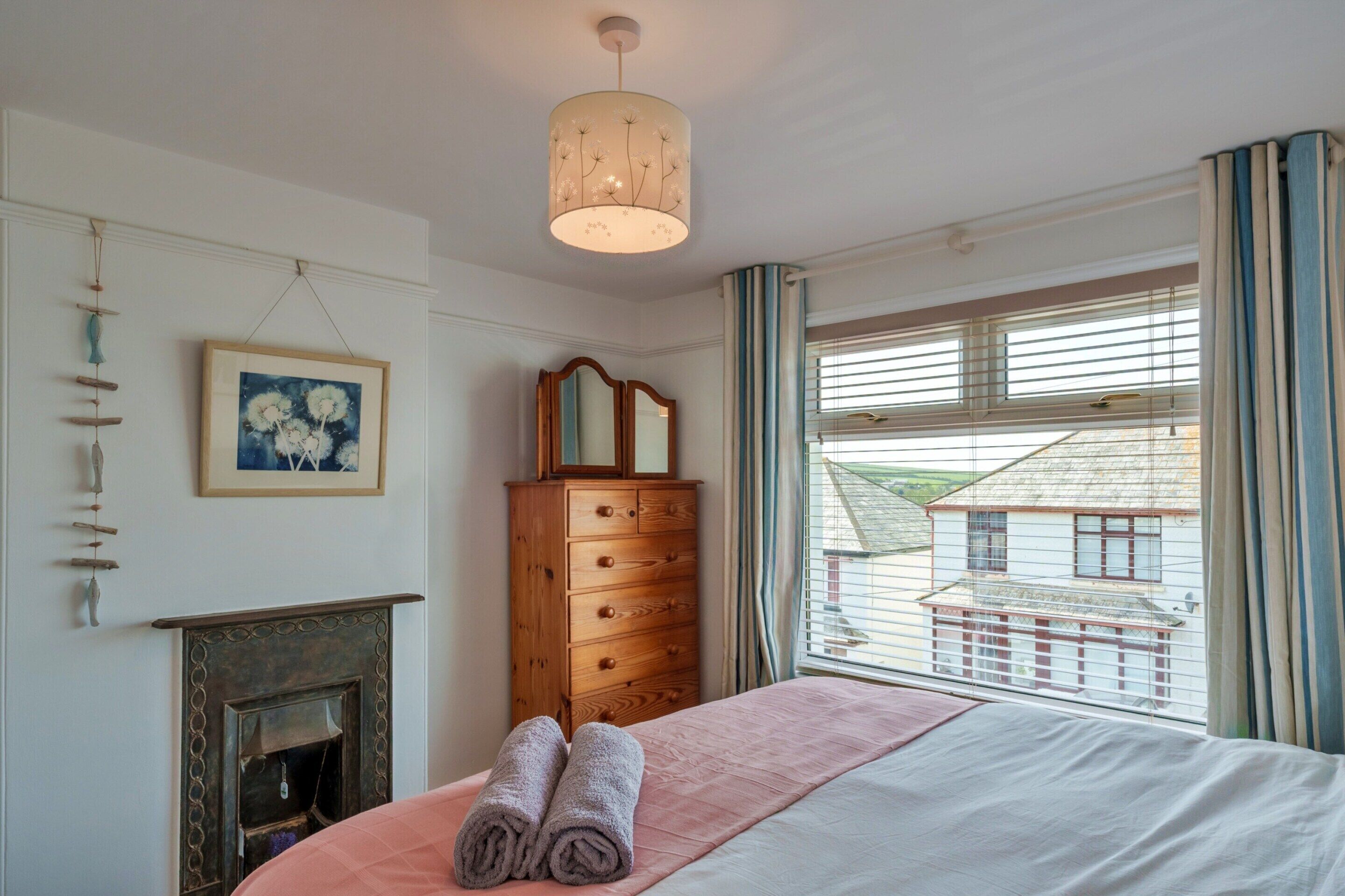 Un dormitorio con cama, cómoda, cuadro, chimenea y ventana con cortinas.