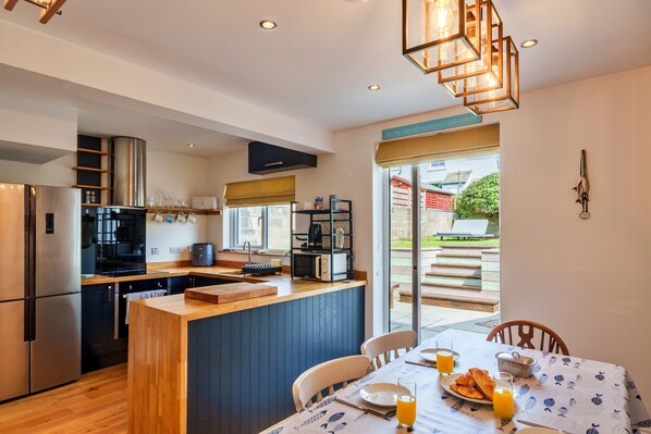 A modern kitchen with a central island, stainless steel appliances, and a dining area with a table set for breakfast. - Peaceful Lochside Retreat for 4 (Bude)