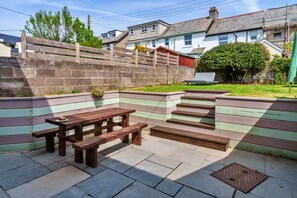 A patio area with a wooden bench and picnic table, surrounded by a low stone wall. - Peaceful Lochside Retreat for 4 (Bude)