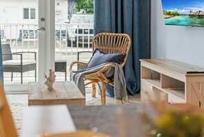 Una silla de mimbre con cojín, una mesa de madera y vistas a un balcón con barandilla.