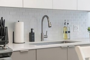 Una cocina moderna con un salpicadero de azulejos blancos, grifo de acero inoxidable y una encimera con dispensador de toallas de papel, dispensador de jabón y una botella de aceite.