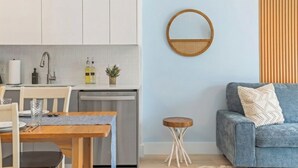 Una cocina moderna con armarios blancos, una mesa de comedor con sillas, un taburete de madera redondo y un sofá azul con un cojín.