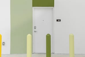 A white door with a numeric sign '107' above it, flanked by two yellow bollards.