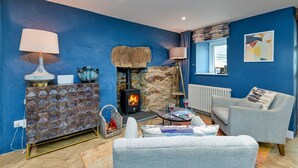 Ein Wohnzimmer mit Kamin aus Stein, einer blauen Wand, einem Fenster mit Blick und einem weißen Sofa.