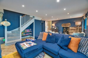 Una sala de estar con un sofá azul, una estantería, una chimenea y una escalera.
