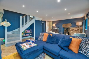 Una sala de estar con un sofá azul, una estantería, una chimenea y una escalera.