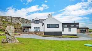 Ein modernes, zweistöckiges Haus mit Steinunterbau, großen Fenstern und einer grünen Vorderfläche.