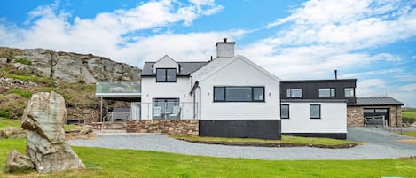 A modern two-story house with a stone foundation, large windows, and a grassy front yard.