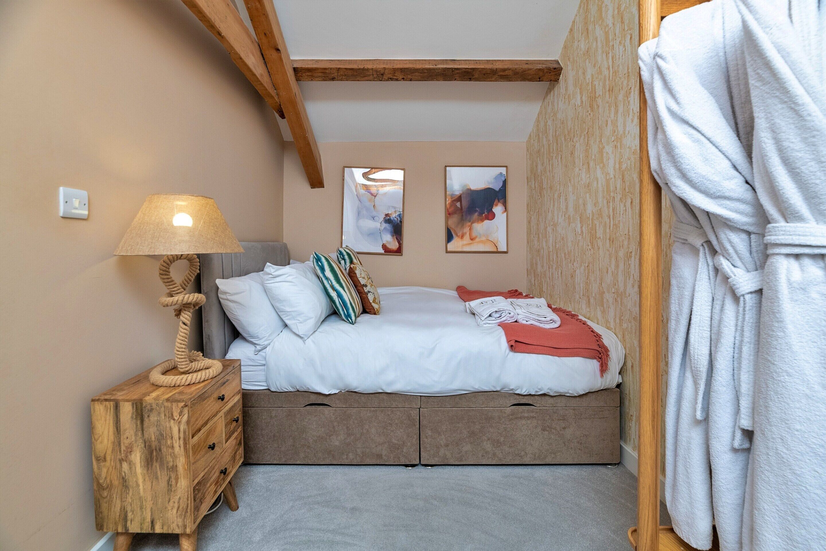 A bedroom with a bed, a wooden nightstand with drawers, a lamp, and a robe hanging on the wall.