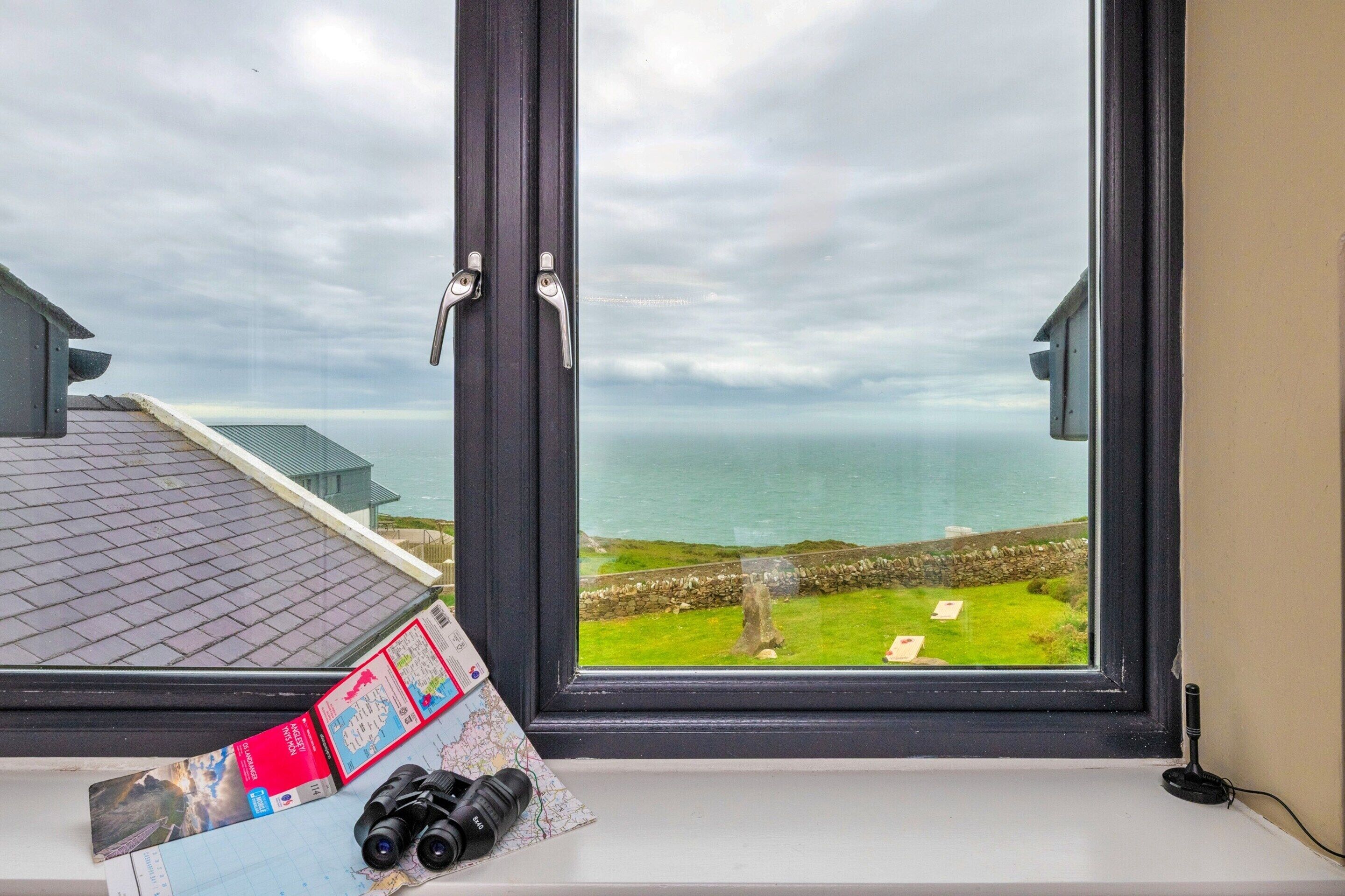 A window with a view of the sea, a map, and binoculars on a windowsill.