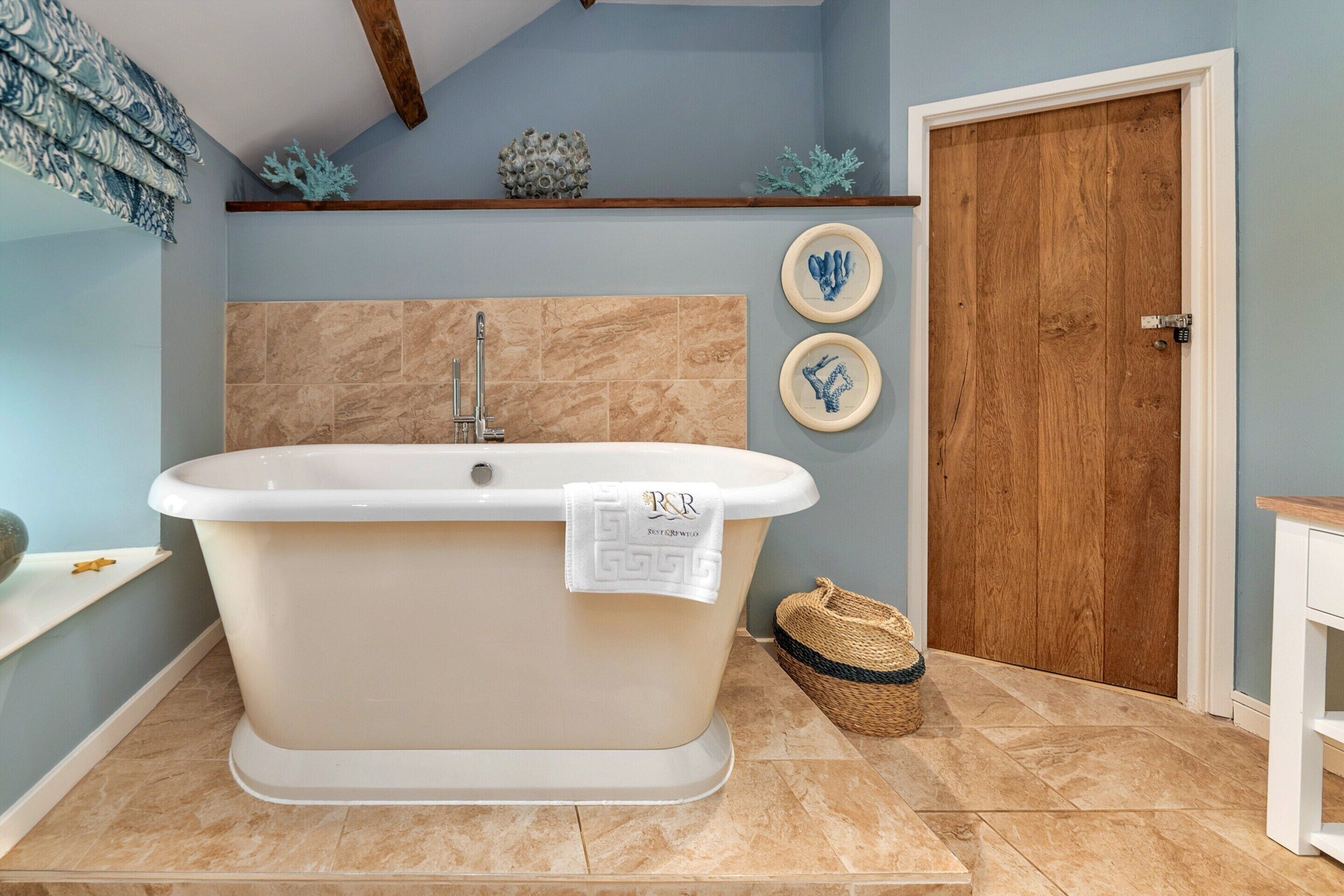 A bathroom with a freestanding bathtub, a wooden door, and two framed wall decorations.