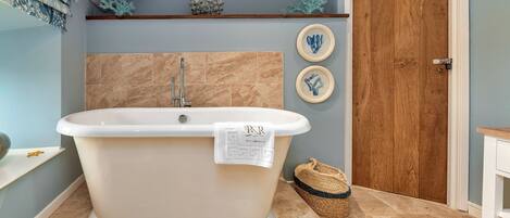 A bathroom with a freestanding bathtub, a wooden door, and two framed wall decorations.