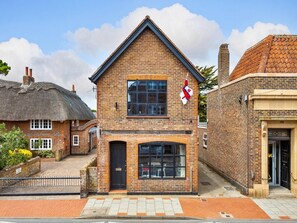 A brick building with a black door and windows, a flag, and a number '152' on the wall. - Selsey Retreat Near the Beach (Chichester)