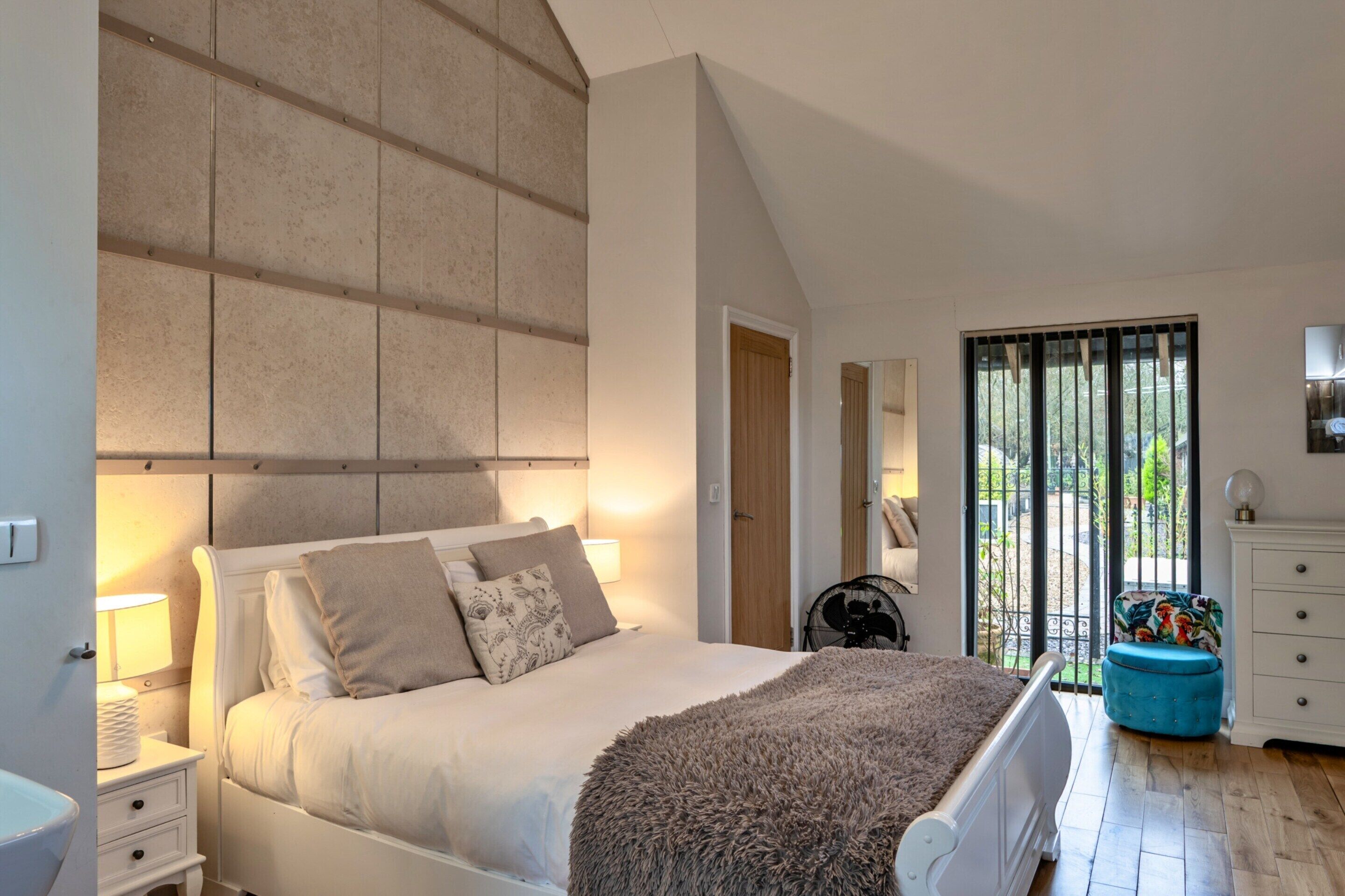 Ein Schlafzimmer mit einem großen Bett, einem Nachttisch, einer Kommode, einem Fenster mit Blick und einer Decke mit freiliegenden Balken.