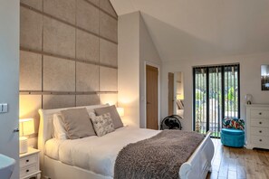 A bedroom with a large bed, a nightstand, a dresser, a window with a view, and a ceiling with exposed beams. - Scenic Hot Tub Cottage for 2 (Wimborne)