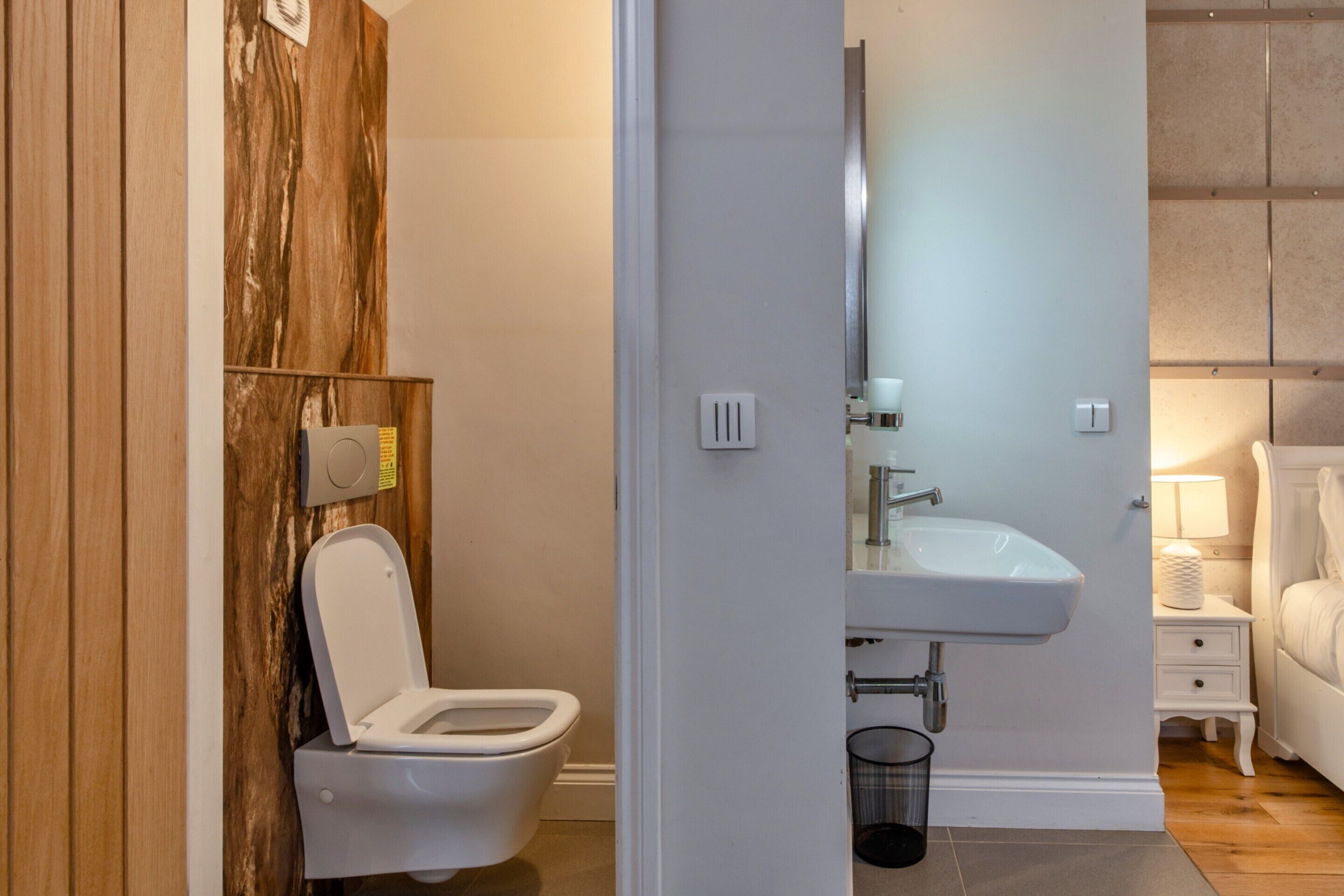 A modern bathroom with a toilet, sink, and a bedside table with a lamp.