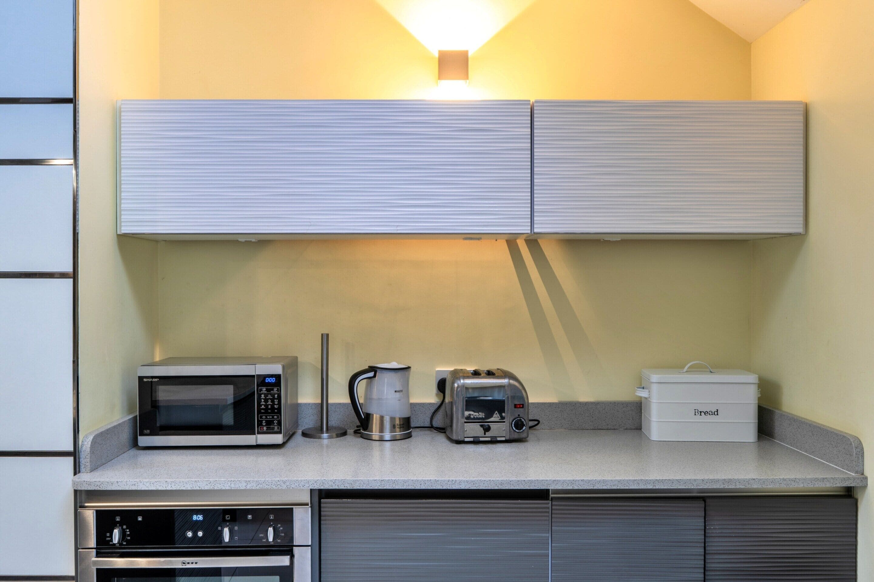 Un angolo cottura con forno a microonde, macchina del caffè, tostapane e spazio per conservare il pane.