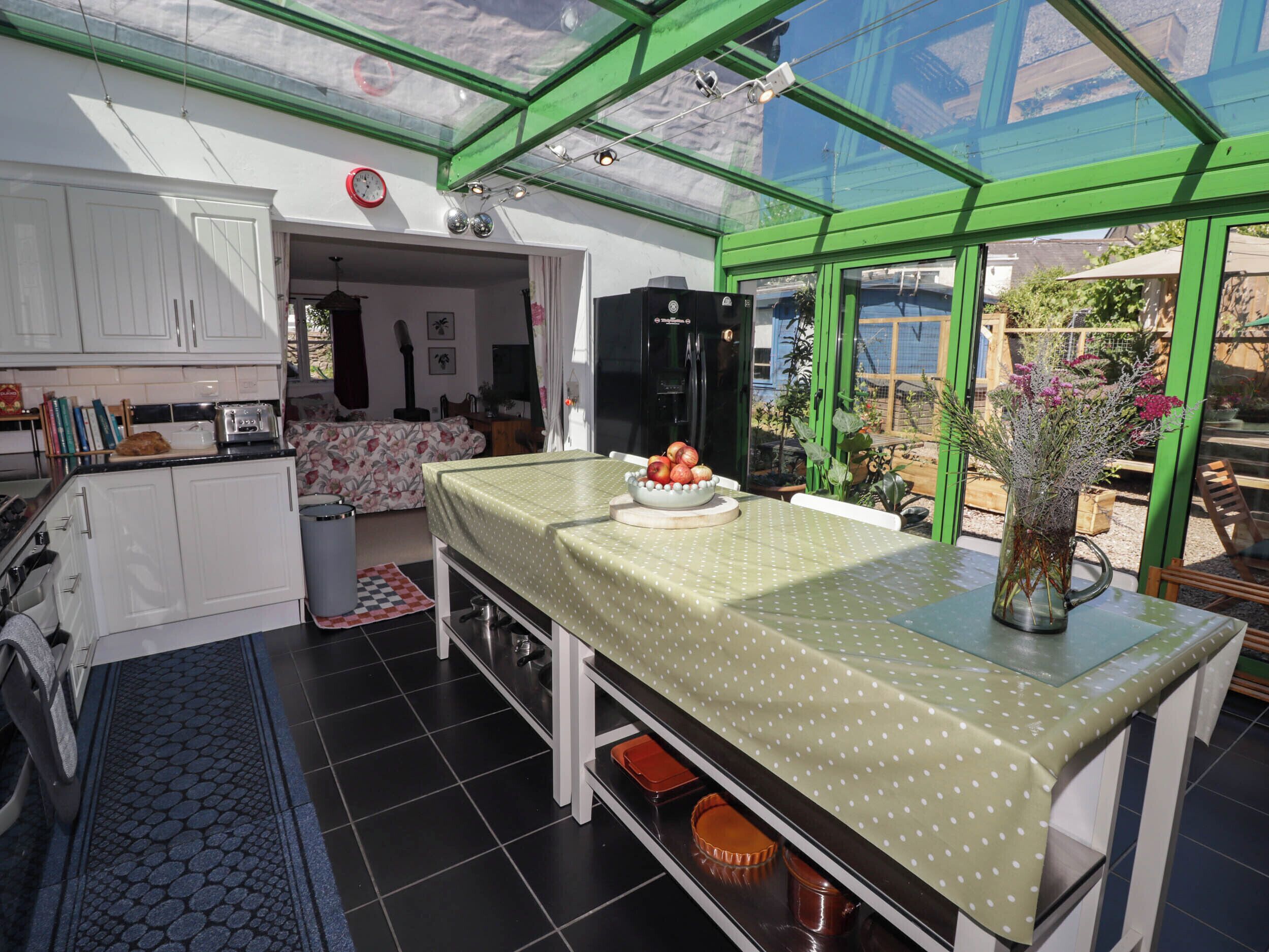 Una cocina con comedor, un reloj a la vista y vistas del jardín a través de un ventanal.