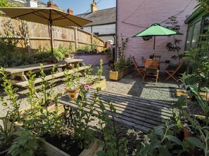 A patio with wooden furniture, potted plants, and a green umbrella. - The Garden Rooms (Narberth)
