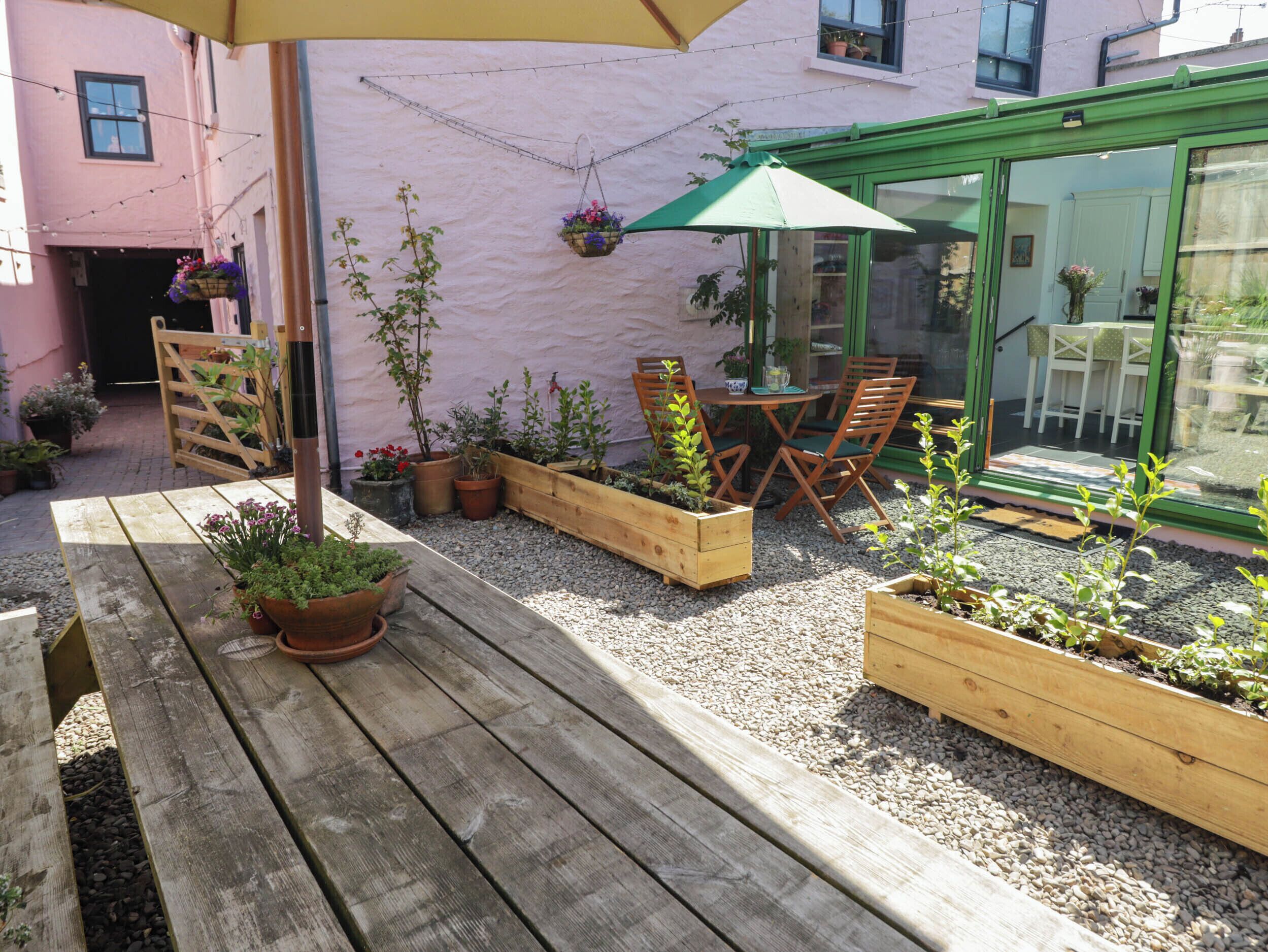 A wooden deck with a table and chairs, surrounded by raised garden beds with various plants.
