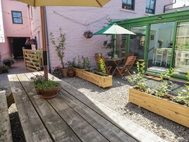 A wooden deck with a table and chairs, surrounded by raised garden beds with various plants.