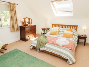 A bedroom with a bed, a dresser, a nightstand, a window with curtains, and a skylight. - The Garden Rooms (Narberth)