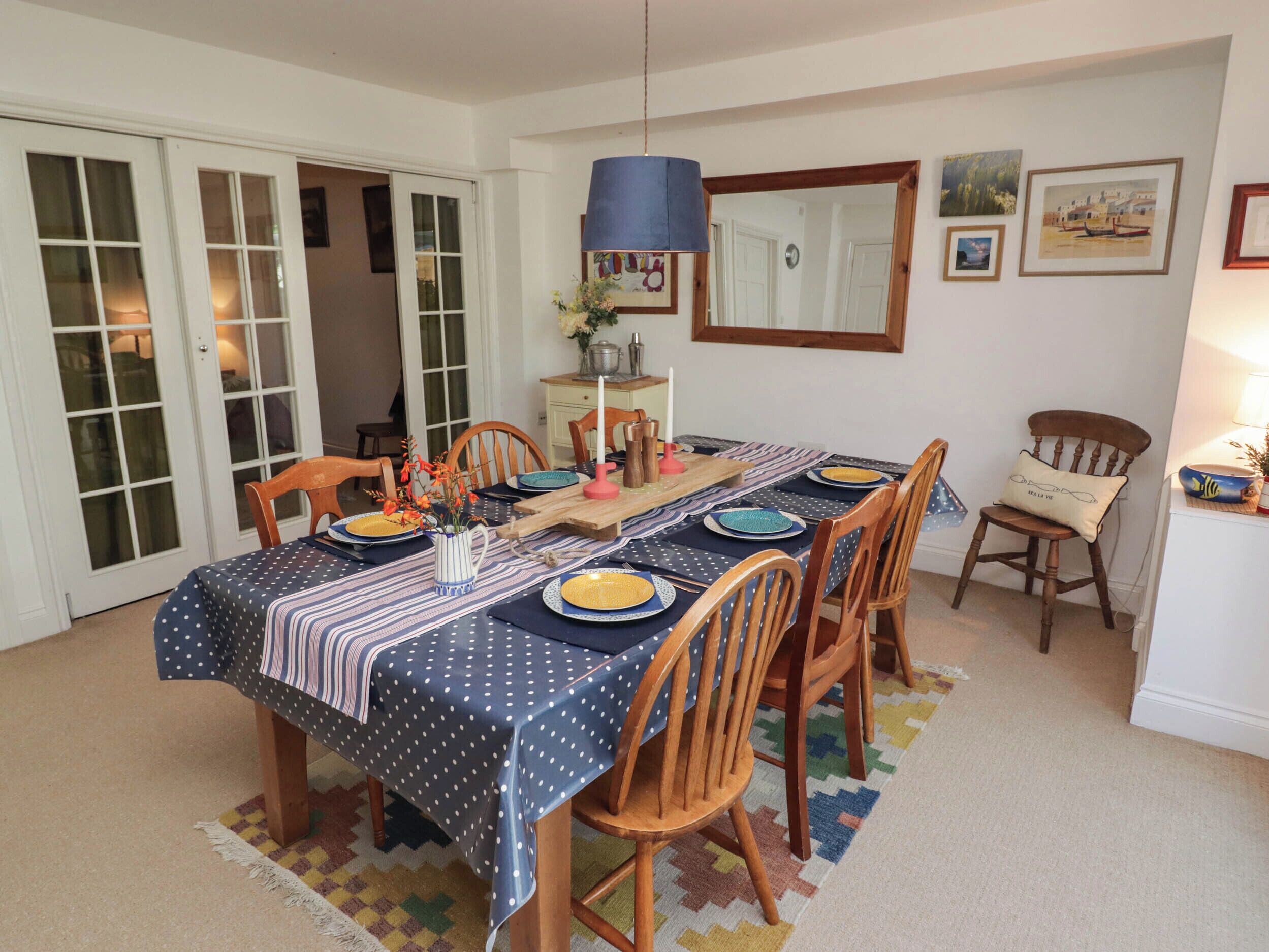 Comedor con una mesa dispuesta para cuatro personas, sillas de madera, mantel estampado y una lámpara colgante azul.