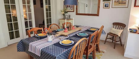 A dining area with a table set for four, surrounded by wooden chairs, a patterned tablecloth, and a blue hanging lamp.