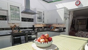 A kitchen with white cabinets, a stove, and a bowl of apples on a table. - The Garden Rooms (Narberth)