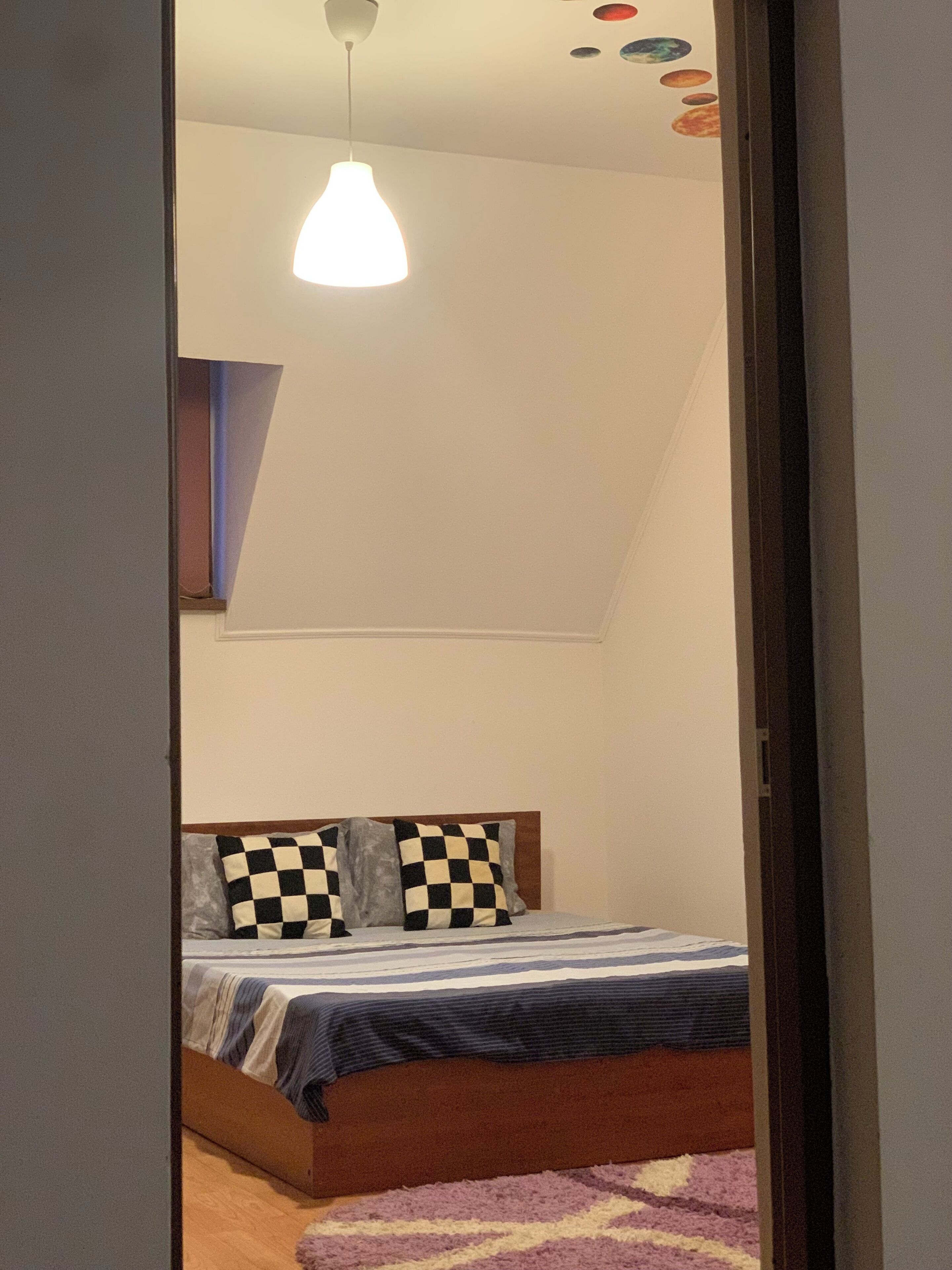 Une chambre à coucher avec un lit, des coussins à motifs à carreaux, un luminaire suspendu et un mur orné de décorations circulaires.
