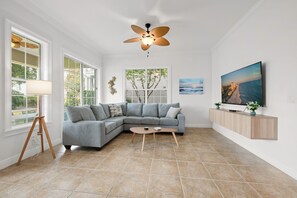 A modern living room with a sectional sofa, a ceiling fan, a television, and a large window. - Minions - Arcade - Guest House - Villa - Pool & Spa 7521 (Kissimmee)