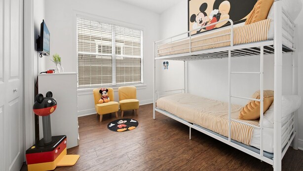 Ein Kinderzimmer mit Etagenbetten, einem Mickey Mouse-Poster, einem Fernseher und einer Mickey Mouse-Spielzeugfigur.