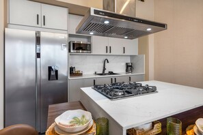 A modern kitchen with a stainless steel refrigerator, a built-in microwave, a gas stove, and a range hood. - Moderno y Acogedor/Capcana/1Br+1Mezzanine (Punta Cana)