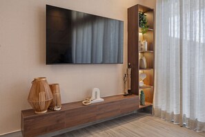 A modern living room with a flat-screen TV mounted on the wall, a wooden console table with decorative items, and a plant on a shelf. - Moderno y Acogedor/Capcana/1Br+1Mezzanine (Punta Cana)