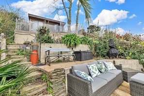 A patio area with a wicker sofa, a table, and chairs. There is a stone wall and a variety of plants. - Estuary View Fowey Cottage for 6 (Fowey)