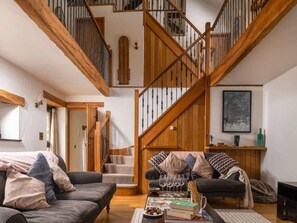 A spacious living area with a wooden staircase, a sofa set, and a coffee table with books and glasses. - Retreat With Valley-view Deck (Ilfracombe)