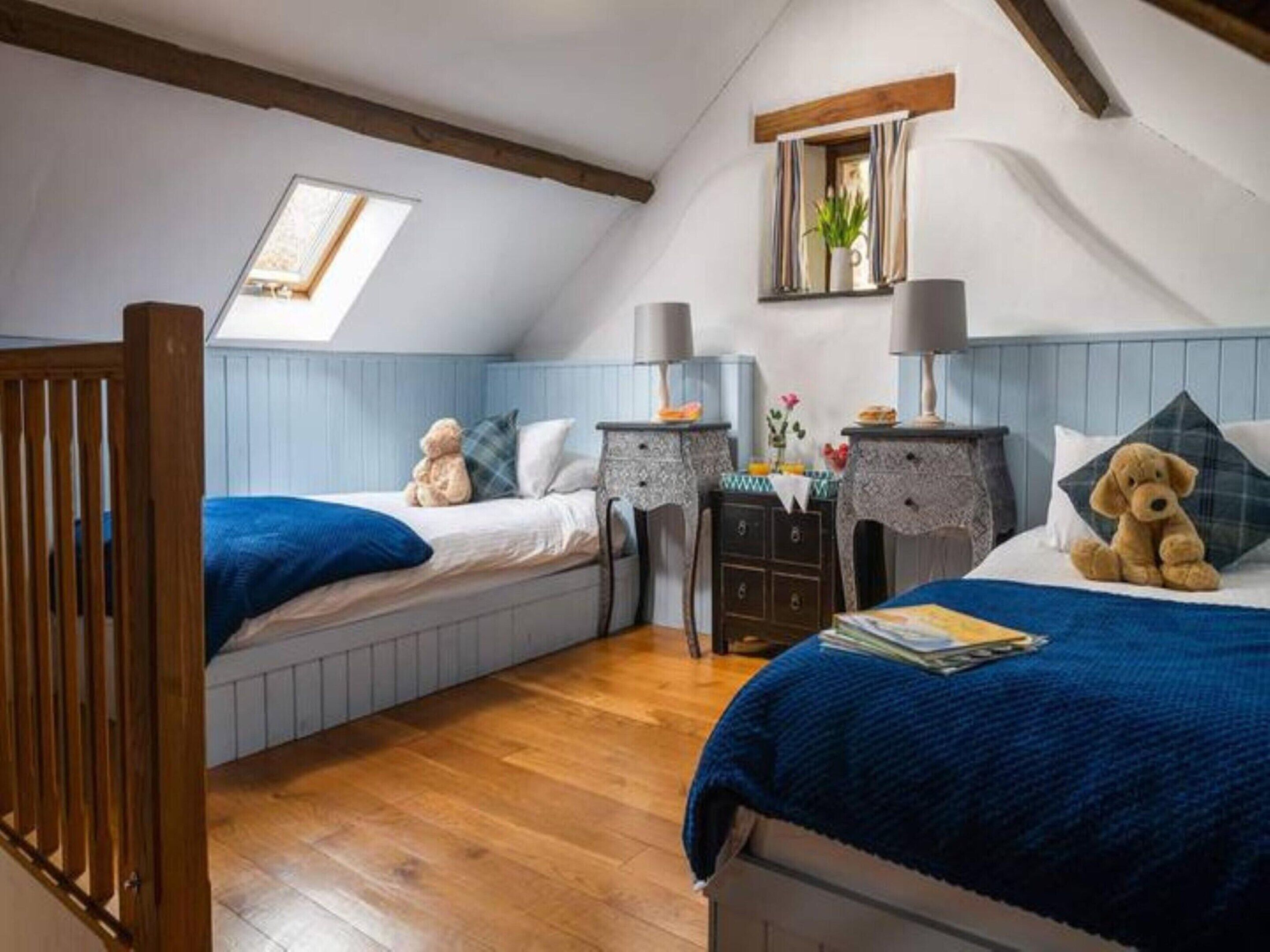 Une chambre avec deux lits, un plancher en bois, un puits de lumière et une fenêtre avec des rideaux.